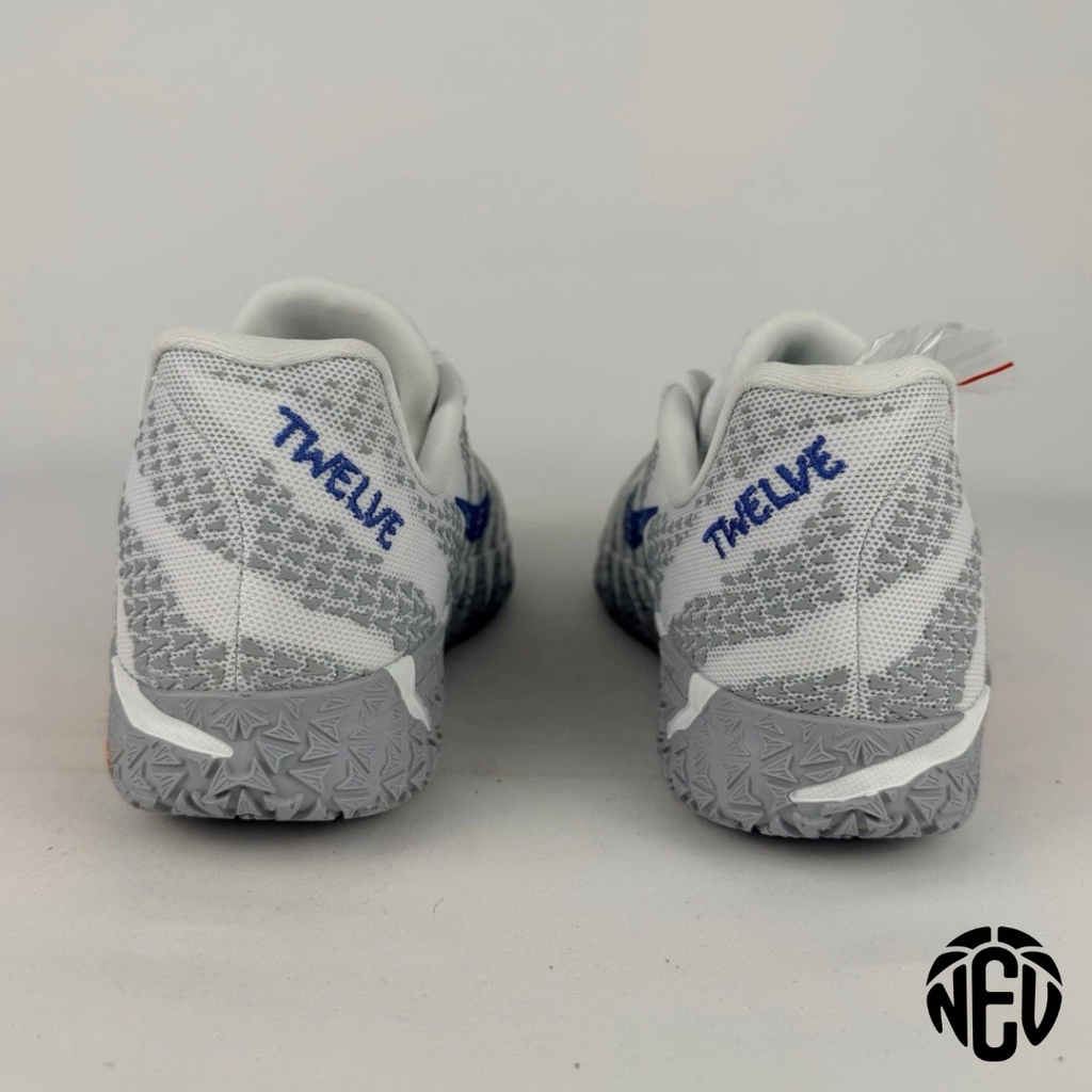 A pair of gray and white athletic sneakers shown from the back, featuring a textured knit upper, white swoosh-like side panels, and blue 'TWELVE' branding on the heel area.